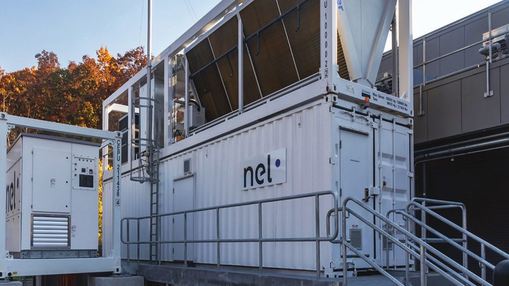 Exterior containerised electrolyser units at the Nel Hydrogen facility, with autumn trees behind.